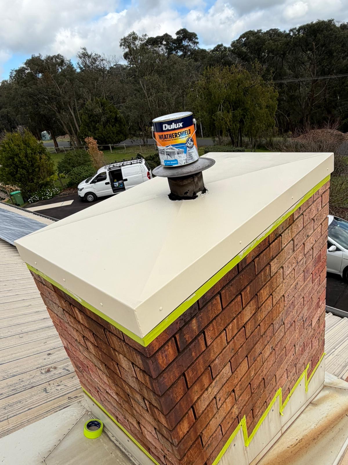 Brick chimney with a finished cream pyramid metal cap on a corrugated metal roof